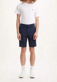 Mörkblå bomullsshorts med rak skärning, med framfickor och knappstängning, bärs med en enkel vit t-shirt och vita sneakers.