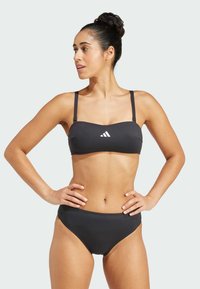 Čierny bikiny set s bandeau vrchným dielom a nastaviteľnými popruhmi, navyše s vysokým pásom. Hladká textúra s bielym logom.