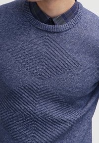 Suéter de punto azul con un patrón geométrico texturizado en el pecho, con un cuello redondo acanalado y un acabado suave y liso.