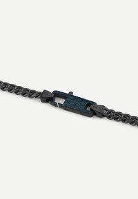 Bracelet en chaîne noir en métal avec un fermoir à motif bleu et noir arborant le logo "GUESS" et une finition texturée.