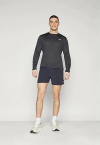 Fekete, hosszú ujjú sportpóló és sötétkék rövidnadrág, amelyen egy diszkrét logó található a mellrészen. Fehér sportcipővel viselve.