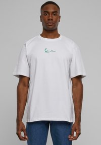 White cotton t-shirt with short sleeves, featuring a green cursive logo on the chest. Simple, relaxed fit with a crew neckline.