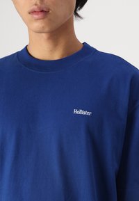 Blue cotton t-shirt featuring a crew neckline and short sleeves, with a small white "Hollister" logo on the left chest area.