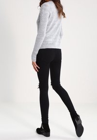 Grå stickad tröja med långa ärmar, kombinerad med svarta rivna skinny jeans och svarta ankelstövlar, med en texturerad finish och subtila detaljer.