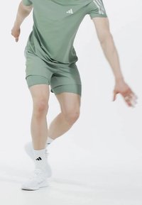 Conjunto atlético de color verde claro que incluye una camiseta de manga corta y pantalones cortos. Zapatillas blancas con detalles negros y calcetines blancos hasta la mitad de la pantorrilla.