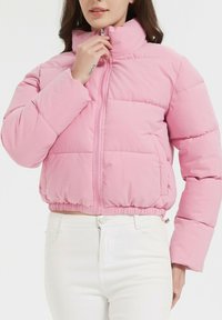 Doudoune rose avec un col montant, fermeture éclair à l'avant et ceinture élastique. Fabriquée en tissu lisse avec des motifs matelassés.