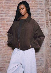 Giacca bomber in ciniglia marrone con collo a camicia e polsini elasticizzati, abbinata a pantaloni della tuta grigi. Tessuto strutturato con vestibilità comoda.