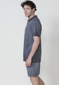 Polo gris texturé avec col, associé à un short assorti. Les deux ont une coupe décontractée et un motif en tricot gaufré subtil.