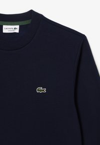 Felpa blu navy con collo a girocollo a costine. Presenta un logo di coccodrillo verde ricamato sul petto. Design a vestibilità classica.