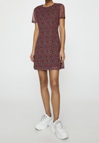 Robe à manches courtes florale avec un fond noir, imprimés rose et vert, longueur au-dessus du genou, associée à des baskets blanches chunky.