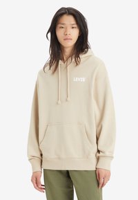Sudadera de algodón beige con un bolsillo frontal, capucha con cordón y el logo blanco "LEVI'S". Presenta un ajuste relajado y puños acanalados.