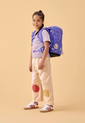 Purple backpack with patterned design, beige pants featuring colorful patches, and white shoes with red stripes. Simplistic, functional style.
