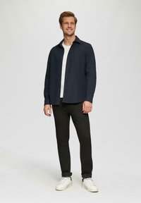 Marineblauwe overhem shirt, wit T-shirt, zwarte broek en witte sneakers. Glad, effen kleuren met een klassieke pasvorm en subtiele details.