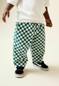 Zeleno-biele nohavice so vzorom kocky, vyrobené z bavlny, doplnené o čierne tenisky s bielymi detailmi a suchými zipsami.