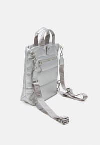 Stříbrná měkká kabelka s lesklým materiálem, horními uchy, nastavitelným popruhem a přední kapsou na zip. Obsahuje kovové kování a detaily s logem.