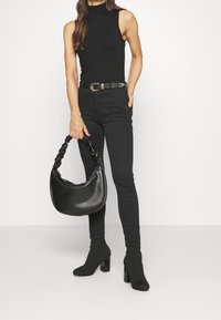 Top negro sin mangas, jeans ajustados negros, cinturón negro con hebilla plateada, botines con tacón negros y un bolso negro texturizado con un asa gruesa.