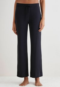Pantalones de pierna ancha en color azul marino, confeccionados en una tela suave, con una cinturilla elástica y cordón ajustable, y dobladillos enrollados en los tobillos.