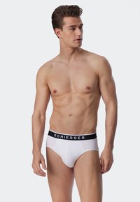 Slip bianchi da uomo con elastico nero che presenta il marchio "SCHIESSER" in bianco. Il tessuto appare liscio e aderente.