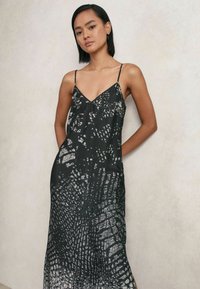Schwarzes ärmelloses Kleid mit V-Ausschnitt, das ein strukturiertes silbernes Muster aufweist, das zerbrochenen Oberflächen ähnelt. Leichter, fließender Stoff.