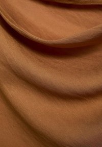Ruskea kangas, jossa on pehmeä ja sileä rakenne, hienovaraisilla viistoreunoilla. Kangas on laskostettu, ja pinnalla leikkii valo.