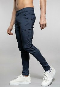 Tmavě modré slim fit kalhoty z texturované látky, s předními kapsami a jedním knoflíkovým zapínáním, v kombinaci s b ílými teniskami.