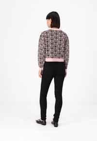 Kurzes Sweatshirt mit pinkem Grund und schwarzem Herzmuster, kombiniert mit schwarzen Skinny-Jeans und schwarzen Ballerinas, von hinten gezeigt.