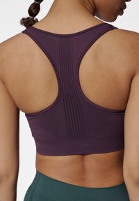 Fioletowy stanik sportowy z designem racerback, z teksturowanym panelem i dopasowanym krojem. Dolny brzeg jest bezszwowy i elastyczny.