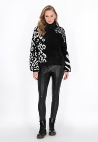 Pulover negru, pufos, cu guler înalt, având modele contrastante de leopard alb și dungi. Asortat cu leggings negri strălucitori și cizme negre cu șireturi.