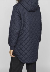 Granatowy pikowany długi płaszcz z kapturem, z wzorem w romby, ściągaczami przy rękawach i zakrzywionym dołem, wykonany z gładkiego, lekkiego materiału.