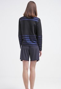 Suéter negro con rayas azules en el reverso, combinado con pantalones cortos oscuros. Textura suave, ajuste casual y tejido ligero.