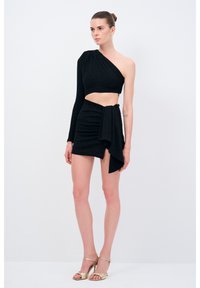 Černý crop top na jedno rameno spárovaný s mini sukní s vysokým pasem a drapovanými detaily. Materiál má jemný lesk.