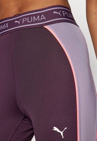Puma leggings sötét lila színben, világoskék és rózsaszín oldalsávokkal. Jellemzője a logó az alsó lábszáron és egy széles derékpánt a márkanevével.