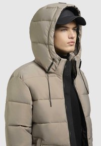 Beige opdrevet jakke med hætte, med en lynlåset front, justerbare snore og vandret quiltet design. Sort indre lag synligt.