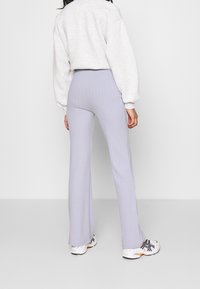 Ljust lila ribbade utsvängda byxor med en åtsittande midja, tillsammans med en grå oversized sweatshirt och vita sneakers.