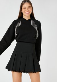 Sudadera negra con detalles de flecos plateados en los hombros, combinada con una falda negra plisada con un dobladillo de encaje. Ambos artículos están hechos de un tejido suave.