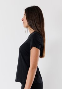 T-shirt nera a maniche corte con scollatura rotonda, texture liscia e vestibilità rilassata, indossata da una persona in profilo su uno sfondo bianco.