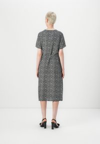 Vestido floral em preto e branco até ao meio da perna, com um corte solto, mangas curtas e cintura ajustada. Usado com sandálias de salto bloco pretas.