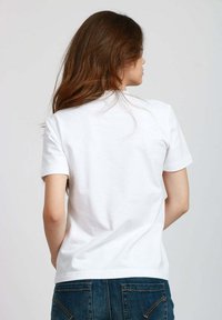 T-shirt bianco in cotone con scollatura rotonda e maniche corte, caratterizzato da una texture liscia e un design semplice. Indossato con jeans in denim blu.