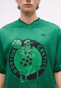 Άτομο που φοράει πράσινη δικτυωτή φανέλα των Boston Celtics με έναν λεπτσαχνού να γυρίζει μια μπάλα του μπάσκετ στο δάχτυλό του.