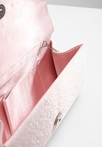 Różowa torebka z satyny o gładkiej fakturze, z srebrnym zapięciem i wnętrzem wyściełanym miękkim różowym materiałem z kieszonką na karty.