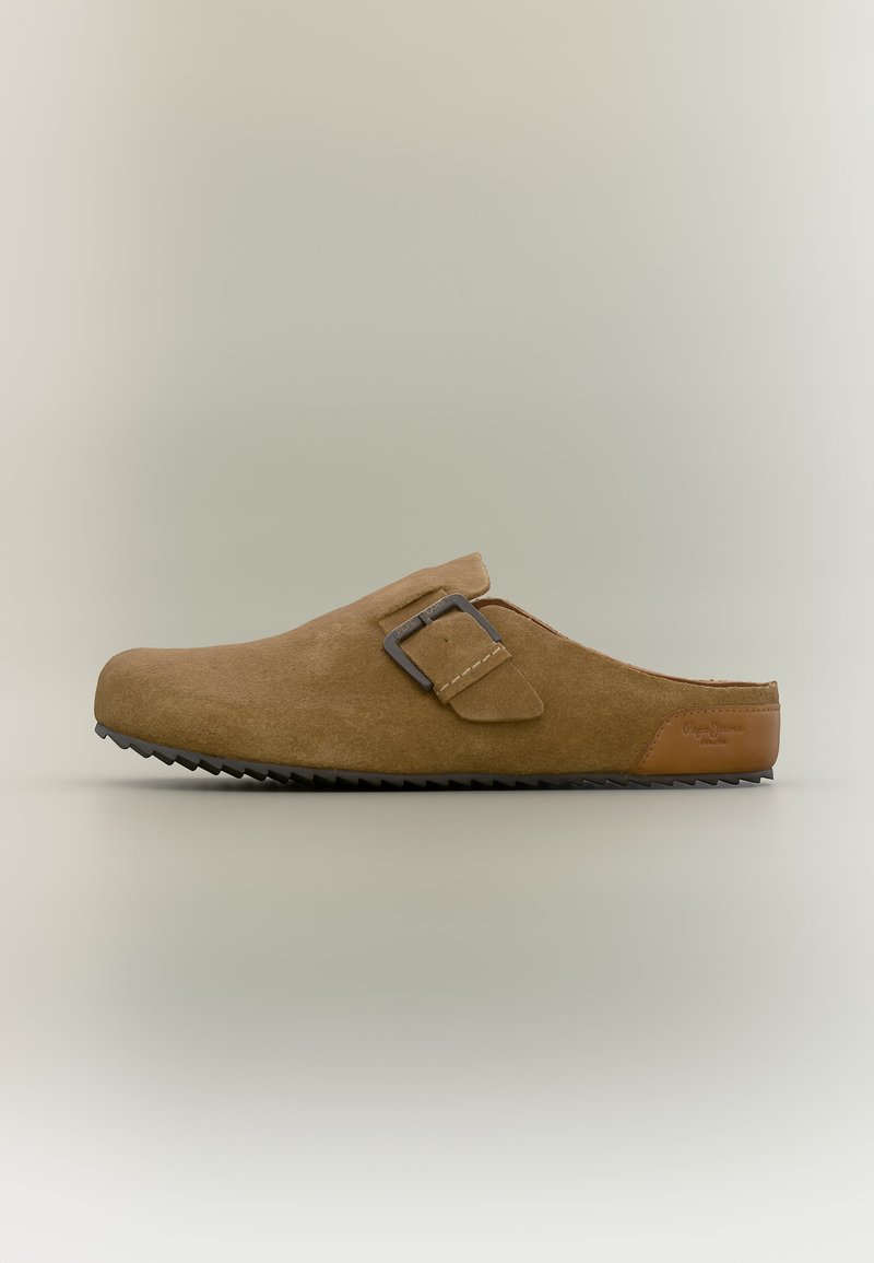 Καφέ σουέτ σανδάλι τύπου κλογκ με ρυθμιζόμενο λουράκι με αγκράφα και αυλακωτή μαύρη σόλα, πλάγια όψη σε ουδέτερο φόντο.