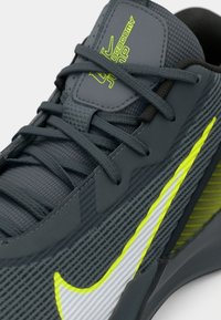 Mørkegrå sneaks med neongul og hvid Nike swoosh, tekstureret mesh-stof og krydsede snørebånd på tungen mærket "Academy".