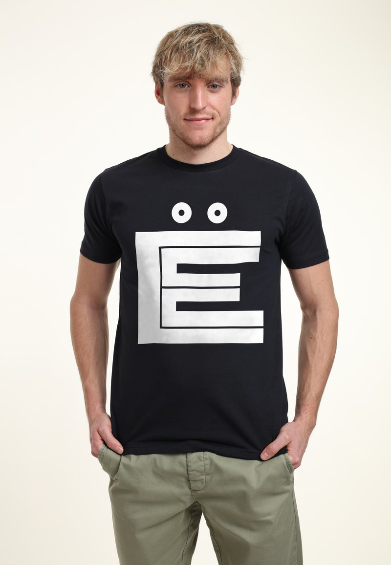Svart t-shirt med kort ärm som har ett stort vitt blockbokstav "E"-motiv med tecknade ögon ovanför. Tillverkad av bomullstyg.