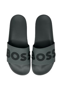 Sandales noires à semelle plate avec une finition mate, présentant une large lanière embossée avec "BOSS" en noir contrasté.