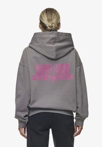 Felpa grigia con un grande grafico testuale rosa che recita "NON SEI PER TUTTI" sul retro; presenta un cappuccio spazioso e polsini a costine.