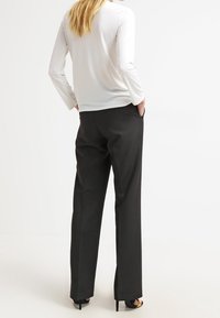 Maglietta bianca a maniche lunghe abbinata a pantaloni neri a vita alta, con taglio dritto e texture liscia, indossata con scarpe nere con tacco alto.