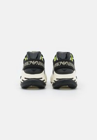 Par svartvita Emporio Armani-sneakers med tjocka sulor, sedd bakifrån mot en enkel vit bakgrund.