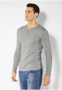 Graues Langarm-Henley-Shirt mit rundem Ausschnitt und drei schwarzen Knöpfen. Der Stoff wirkt weich, enganliegend und mit einer glatten Textur.