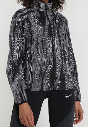 Schwarz-graue Jacke mit Reißverschluss, die ein Wirbelmuster, einen hohen Kragen und leichtes, glänzendes Material aufweist. Kombiniert mit schwarzen Sportleggings.