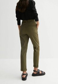Olive green trousers with a straight fit, cuffed hems, belt loops, and side pockets, paired with black strappy sandals.